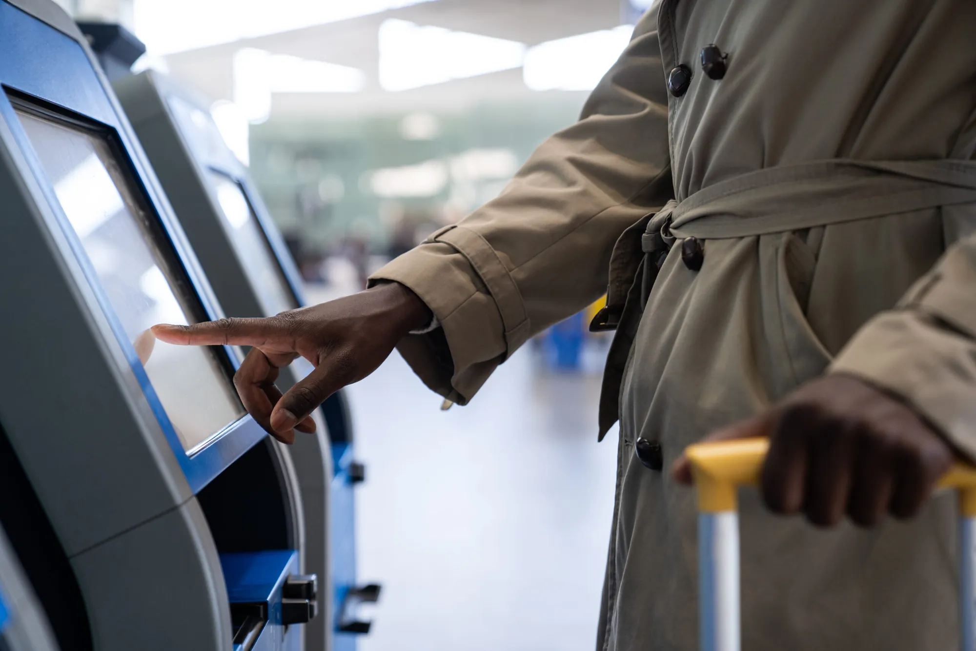 A passenger touching an airport self-service check-in screen, luggage in hand